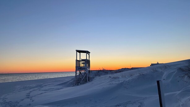 Lumisen rannan reunalla kohoaa rantavalvontatorni, taustalla kirkas taivas ja meri.