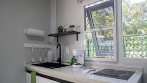 A kitchen with a black faucet, a coffee maker, and a window with a view of greenery. - Coqui Tiny House - Unit 12 (Rincón)