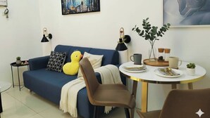 Una sala moderna con un sofá azul, un patito de juguete amarillo, una mesa de comedor con una taza blanca y un cuadro en la pared.