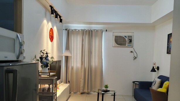 Una sala de estar moderna con una televisión, un refrigerador, un sofá, una mesita y una lámpara.