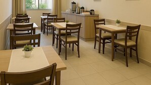 A dining area with multiple tables and chairs, a kitchenette, and a window with curtains. - Pousada La Castaña (Belém)