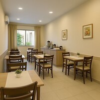 Uma área de refeições com várias mesas e cadeiras, uma cozinha compacta e uma janela com cortinas.