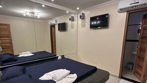 A hotel room with a large bed, a vanity with a mirror, a television mounted on the wall, and an air conditioning unit. - Pousada La Castaña (Belém)