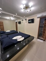 Quarto de hotel com uma cama grande, uma mesa de toucador com espelho, uma televisão na parede e um ar condicionado.