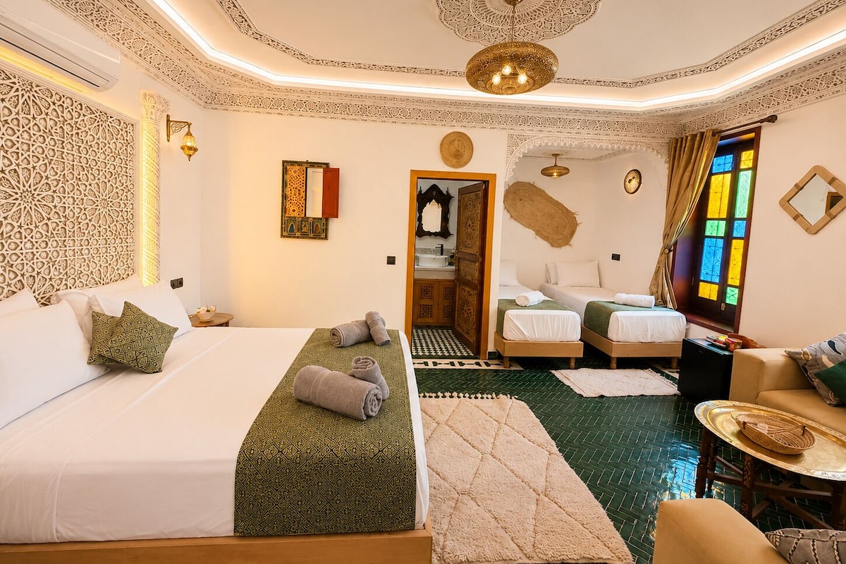 Habitación de hotel con una cama grande, dos camas más pequeñas, un área de estar y un baño.