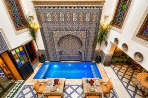 A traditional Moroccan interior with a central swimming pool, ornate tile walls, and a seating area with a table set for two. - Riad Dar Elbellar (Fes)