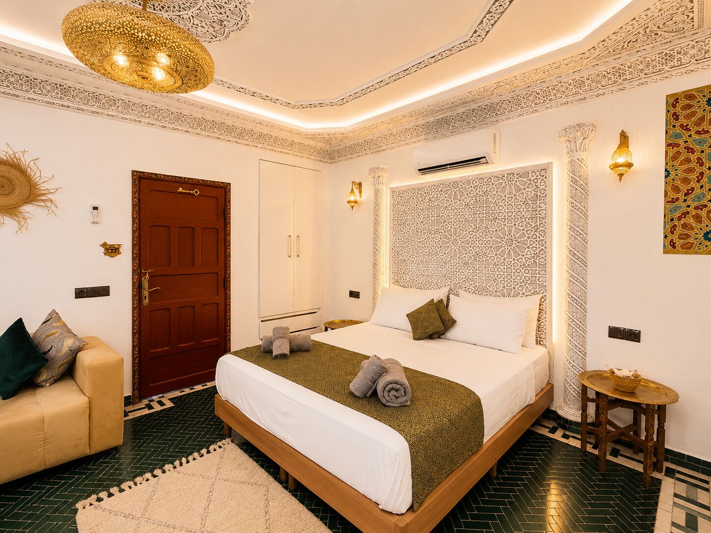 A hotel room with a bed, a sofa, a small table, and a decorative wall.