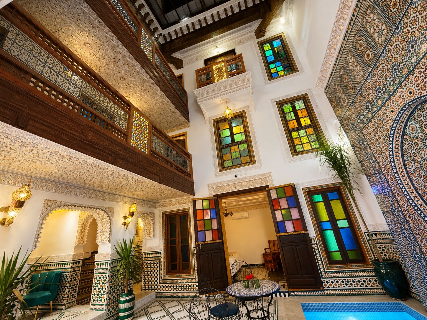 Un interior tradicional con intrincados trabajos de azulejos, un balcón y una zona de estar con mesa y sillas.