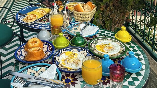 A table set with breakfast items, including eggs, bread, and orange juice, on a patterned tablecloth.