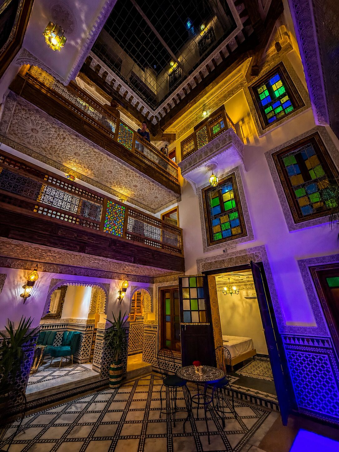 Un interior de varios niveles con balcones ornamentados, paredes con diseños y un suelo de cuadros.