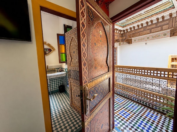 Une pièce dotée d’un sol à carreaux, d’une porte en bois ornée de motifs complexes et d’un balcon avec une balustrade à motifs.