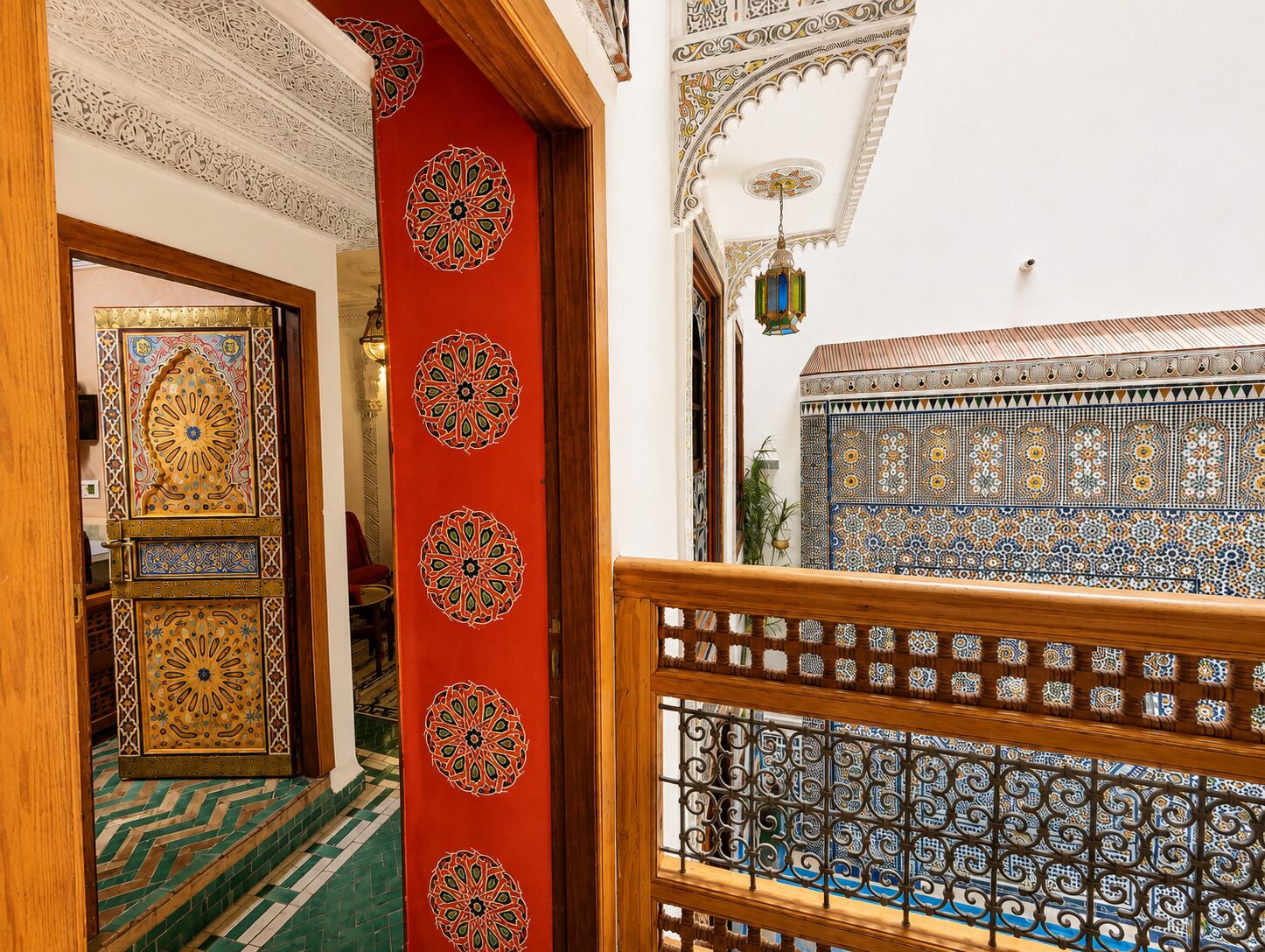 A hallway with intricate tile work, a red decorative panel with circular patterns, and a view of a room with blue and white patterned tiles.