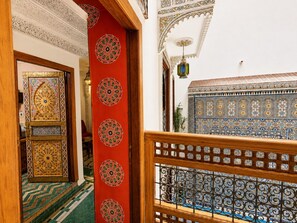 A hallway with intricate tile work, a red decorative panel with circular patterns, and a view of a room with blue and white patterned tiles. - Riad Dar Elbellar (Fes)