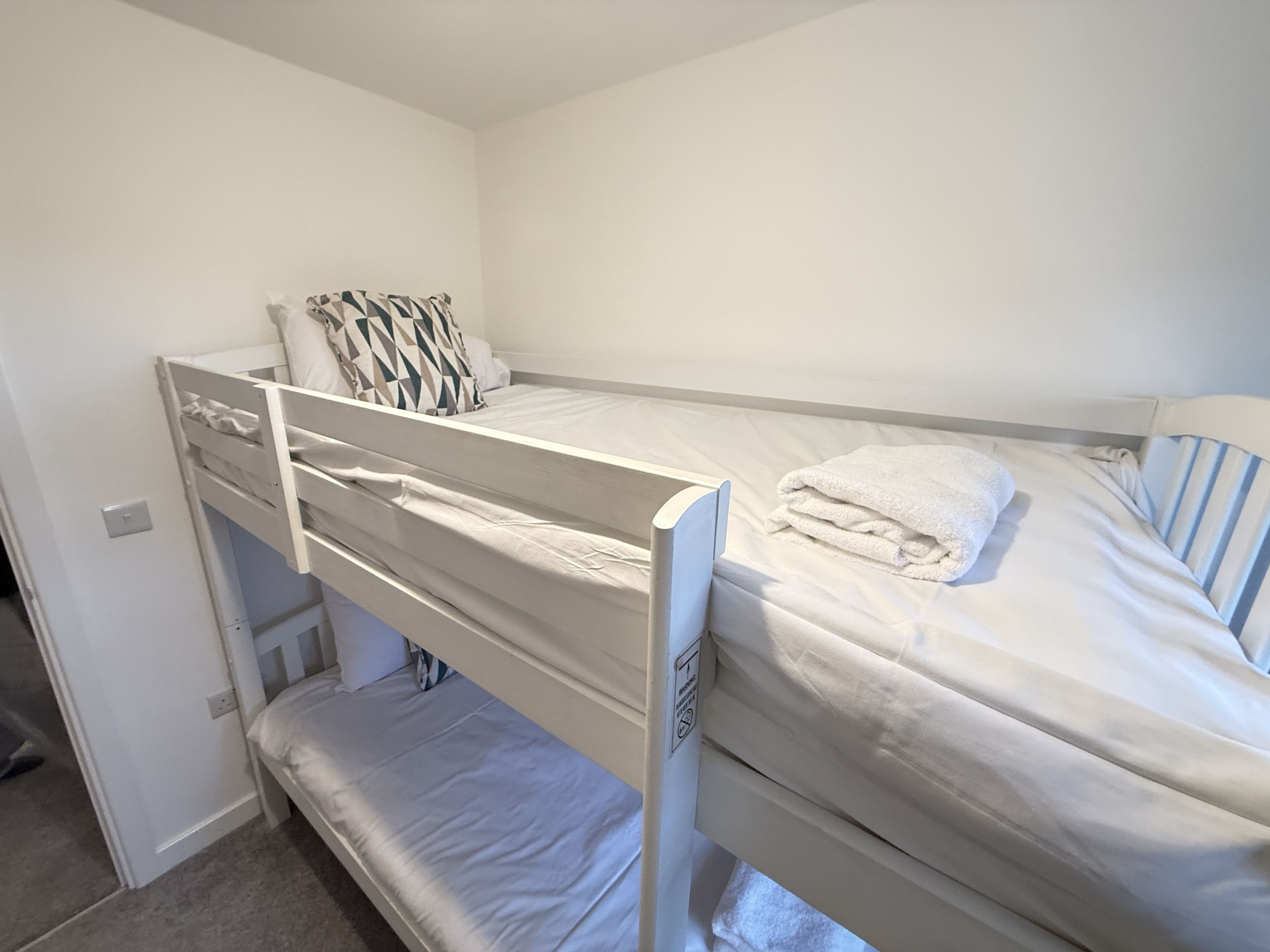 A bunk bed room with white bedding and a striped pillow.