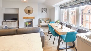 Un salon moderne avec une cheminée, un coin repas avec des chaises bleues, un canapé et un téléviseur posé sur un meuble en bois.