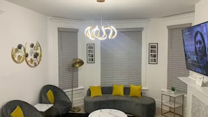 A modern living room with a grey sofa, yellow cushions, a round coffee table, and a television on the wall. - Stunning Home Downtown with free street parking! Sleeps 10 (Columbus)