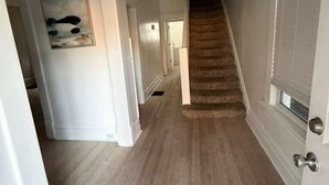 A hallway with a wooden floor, white walls, and a staircase leading to another room. - Stunning Home Downtown with free street parking! Sleeps 10 (Columbus)