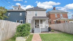 A two-story house with a front porch, a brick chimney, and a wooden fence. - Stunning Home Downtown with free street parking! Sleeps 10 (Columbus)