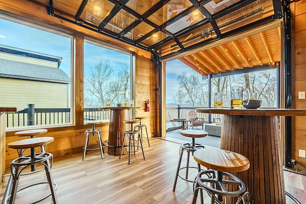 An indoor patio area with wooden flooring, metal bar stools, and tables.