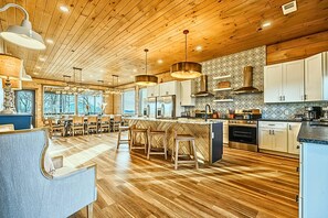 A modern kitchen with wooden flooring, pendant lighting, and white cabinetry.