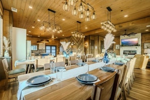 A spacious dining area with wooden tables, hanging light fixtures, and a television mounted on the wall.
