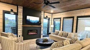 A cozy living room with a fireplace, comfortable seating, and large windows offering a view of the outdoors. - Heated Pool-Mtn View-Game Loft-Waterpark-Sleeps 20 (Sevierville)