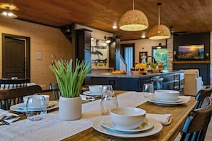 A dining area with a wooden table set for four, a potted plant, and a kitchen in the background. - Heated Indoor Pool · Hot Tub · Theater · Sleeps 20 (Sevierville)