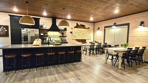 A modern kitchen with a bar area, wooden flooring, and a dining setup with multiple chairs and tables. - Heated Pool-Mtn View-Game Loft-Waterpark-Sleeps 20 (Sevierville)