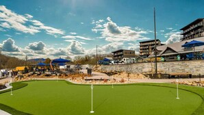 A golf course with a putting green, surrounded by buildings and outdoor seating areas. - Heated Pool-Mtn View-Game Loft-Waterpark-Sleeps 20 (Sevierville)