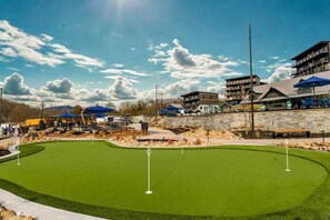 A golf course with a putting green, surrounded by buildings and outdoor seating areas. - Heated Pool-Mtn View-Game Loft-Waterpark-Sleeps 20 (Sevierville)
