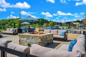 An outdoor patio area with stone fire pit, outdoor furniture, and a pool in the background. - Heated Indoor Pool · Hot Tub · Theater · Sleeps 20 (Sevierville)