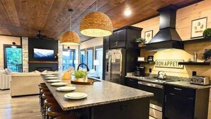 A modern kitchen with a central island, bar stools, a black refrigerator, and a sign that reads "BON APPETIT". - Heated Pool-Mtn View-Game Loft-Waterpark-Sleeps 20 (Sevierville)