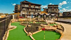 A miniature golf course with a green artificial turf, surrounded by stone walls and large rocks. - Heated Pool-Mtn View-Game Loft-Waterpark-Sleeps 20 (Sevierville)