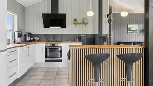 A modern kitchen with white cabinets, a black range hood, and a wooden island with bar stools. - Peaceful holiday dream by the Limfjord coast (Struer)