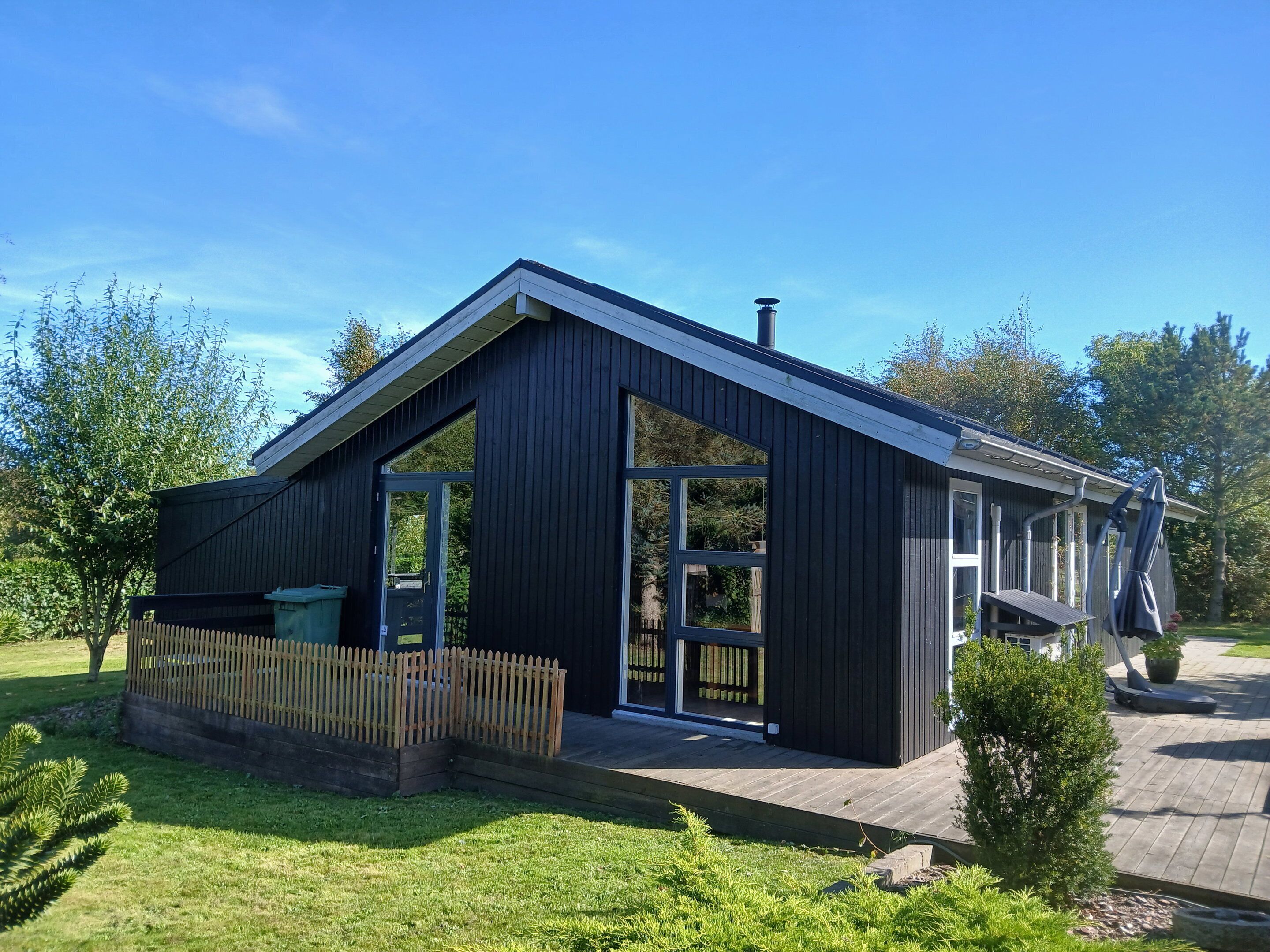 A modern house with a large glass door, a wooden deck, and a fenced yard.