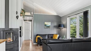 A modern living room with a fireplace, a black leather sofa, and a large window with a view of greenery. - Peaceful holiday dream by the Limfjord coast (Struer)
