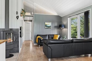 Ein modernes Wohnzimmer mit Kamin, einer schwarzen Ledersofa und einem großen Fenster mit Blick ins Grüne.