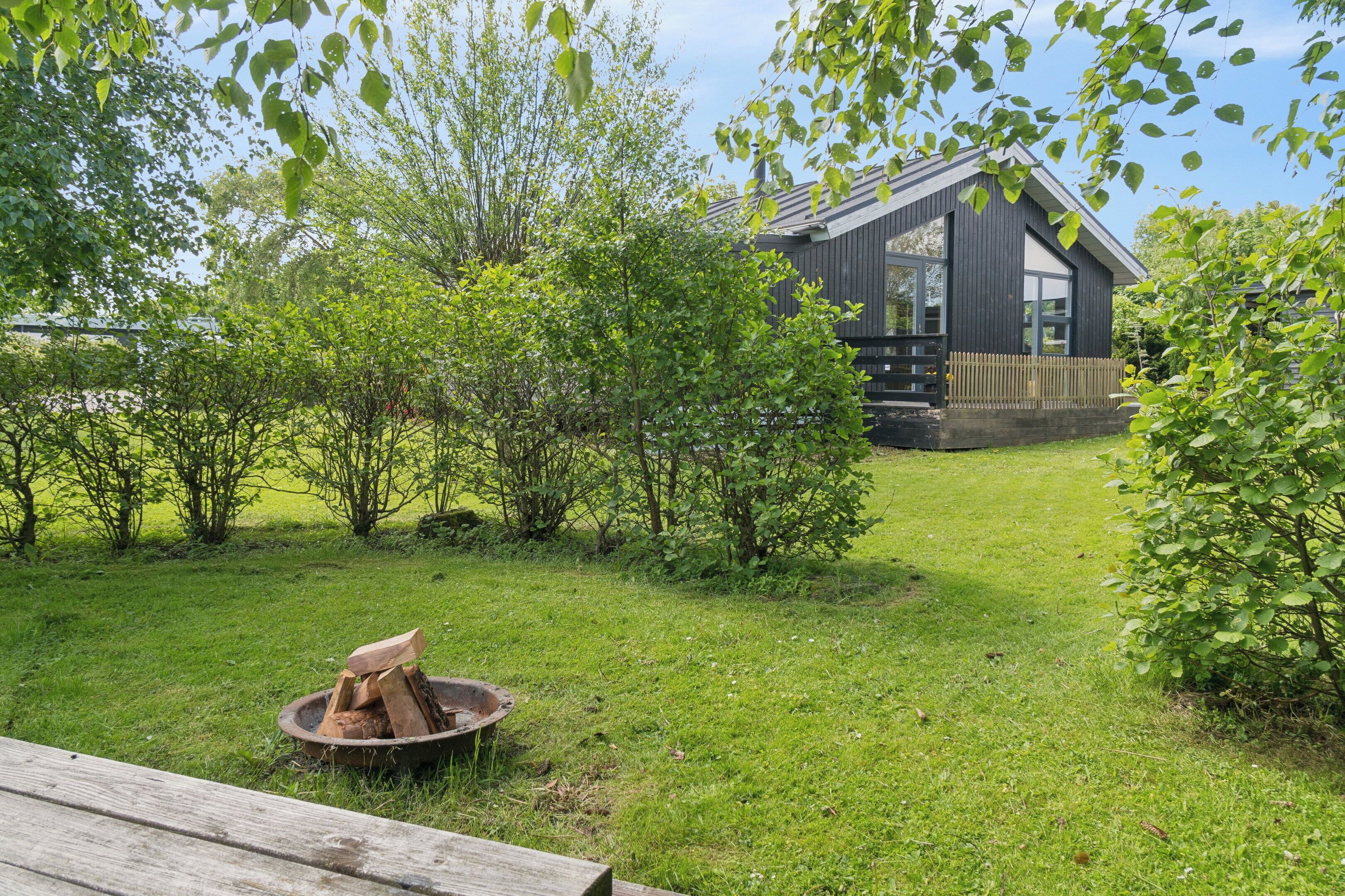 Uma casa moderna com um deck, cercada por vegetação exuberante e uma lareira.