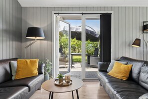 Ein modernes Wohnzimmer mit Ledersofas, einem Couchtisch und einer Glastür, die auf eine Terrasse im Freien führt.