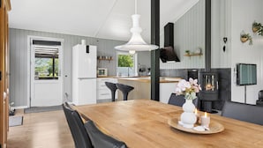 A modern kitchen with a central island, a dining area with a wooden table, and a fireplace. - Peaceful holiday dream by the Limfjord coast (Struer)