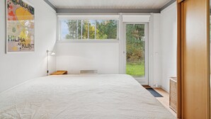 Une chambre avec un grand lit, une fenêtre, une porte et une affiche accrochée au mur.