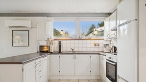 Une cuisine moderne avec des meubles blancs, un four encastré et une fenêtre donnant sur un jardin.