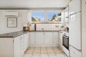 Eine moderne Küche mit weißen Schränken, einem eingebauten Backofen und einem Fenster mit Blick auf einen Garten.