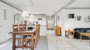 Une cuisine spacieuse avec un coin repas, un salon doté d’un canapé et un couloir menant à une porte.