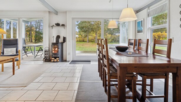 Un vaste espace dédié à la salle à manger, avec une grande table et des chaises, un poêle à bois et de grandes fenêtres offrant une vue sur l’extérieur.