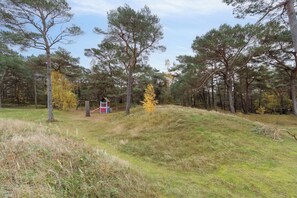Un paysage naturel composé d’arbres, d’une colline herbeuse et d’une petite construction aux couleurs rouge et blanche.