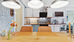 Eine moderne Küche mit weißen Schränken, einem schwarzen Herd und einer Mikrowelle. Ein Esstisch mit Stühlen und eine Blumenvase sind ebenfalls vorhanden.