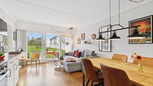 Eine moderne Küche mit weißen Schränken, ein Essbereich mit einem Holztisch und Stühlen sowie ein Wohnzimmer mit einer Couch und einem Couchtisch.