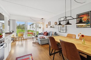 Une cuisine moderne avec des meubles blancs, un coin repas avec une table et des chaises en bois, et un salon avec un canapé et une table basse.