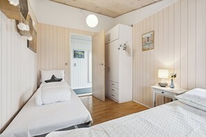 Une chambre avec deux lits, une armoire, une table de chevet avec une lampe et une porte donnant sur une autre pièce.